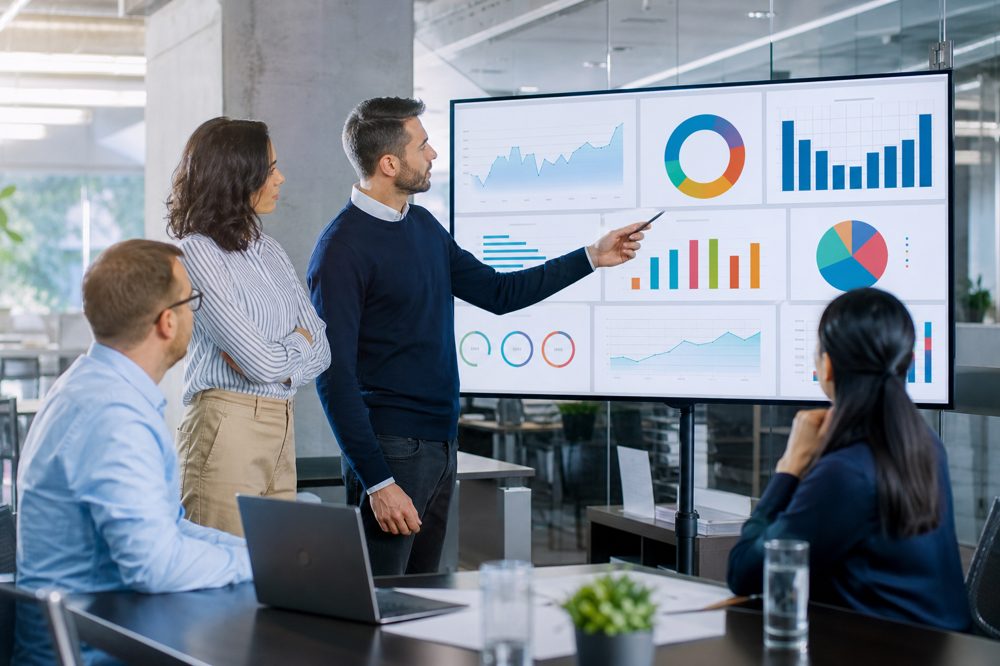 中小企業のチームがオフィスの大型モニターでKPIダッシュボードを分析している場面