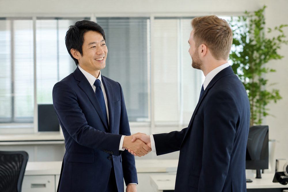 日本人の運送会社管理者と外国人従業員が明るいオフィスで握手をしている採用成功のシーン