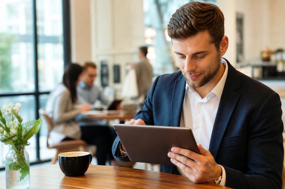 外回り中の営業担当者がカフェでタブレットにCRMデータを入力している場面