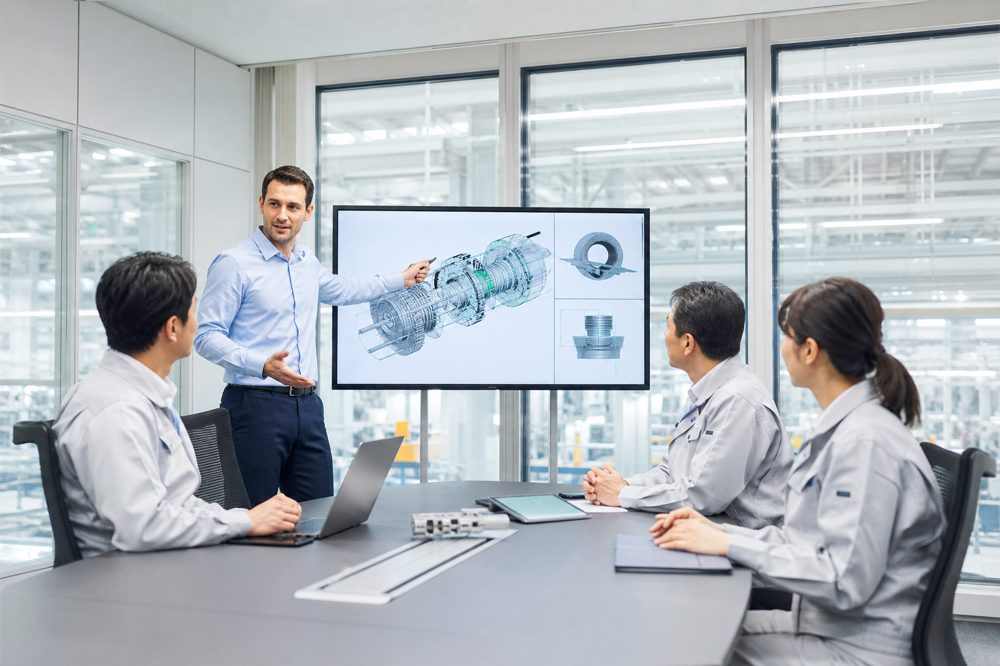 外国人エンジニアが製造会社の会議室で日本人同僚に技術成果をプレゼンしている場面