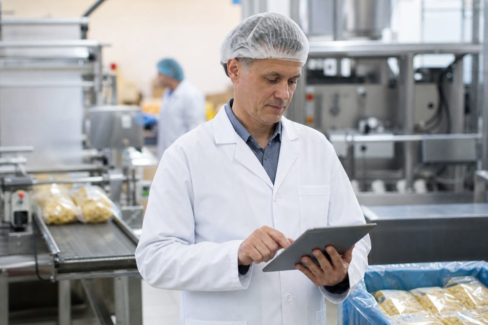 食品工場でタブレットデータを確認する中年の工場長