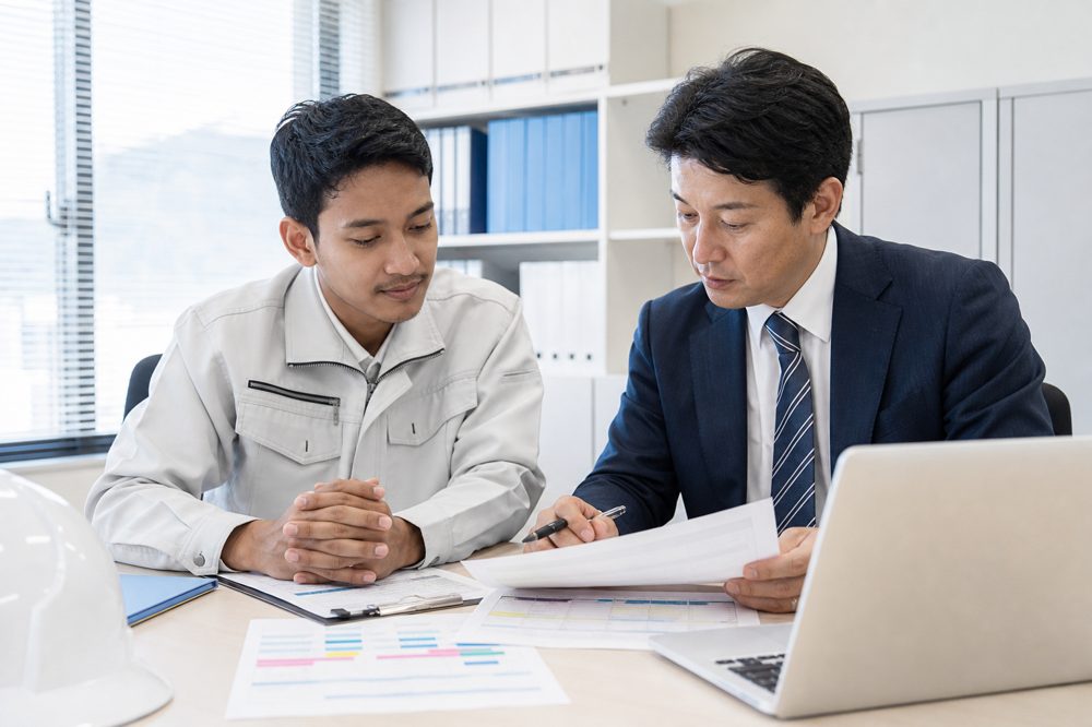 日本の中小企業で書類・スケジュールを確認する日本人担当者と外国人技能実習生