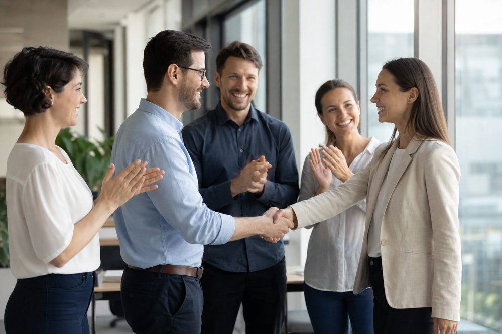 中小企業のチームが新入社員を明るいオフィスで温かく迎えている場面