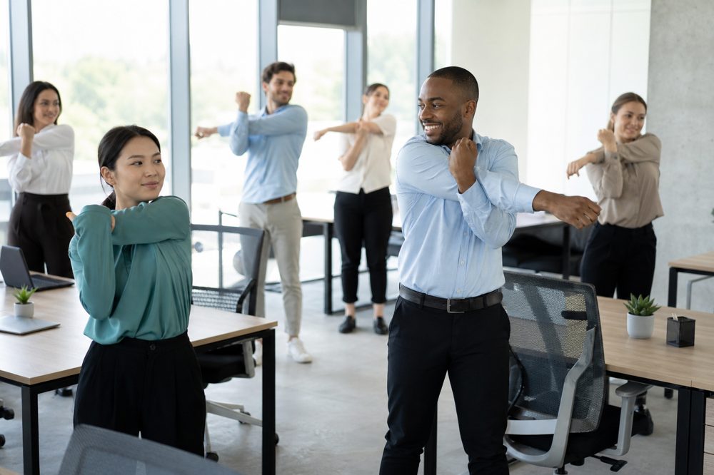企業の従業員が明るいオフィスで一緒にストレッチをしている様子