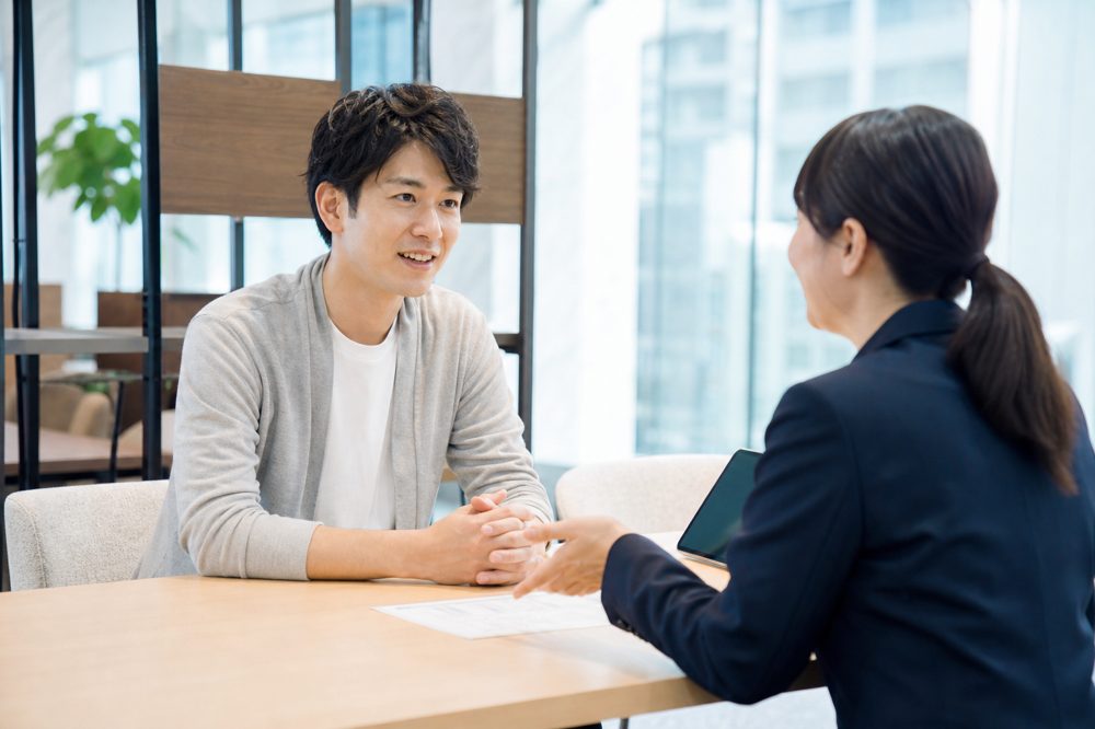 大阪の明るいオフィスで保険アドバイザーに相談する20代の日本人男性