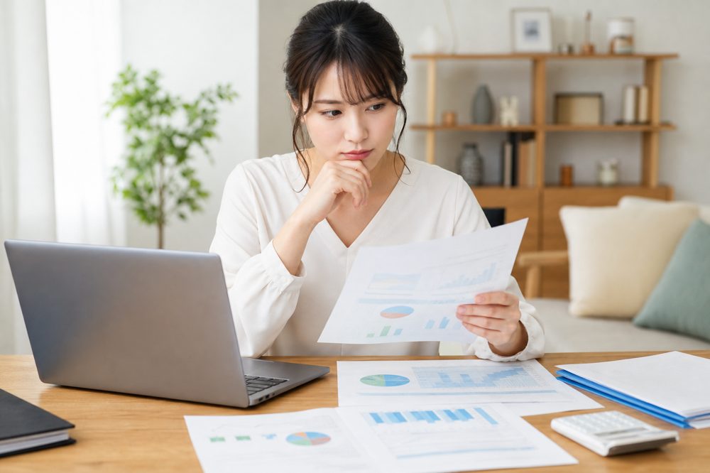 自宅の机で保険の比較資料を真剣に確認する20代の日本人女性