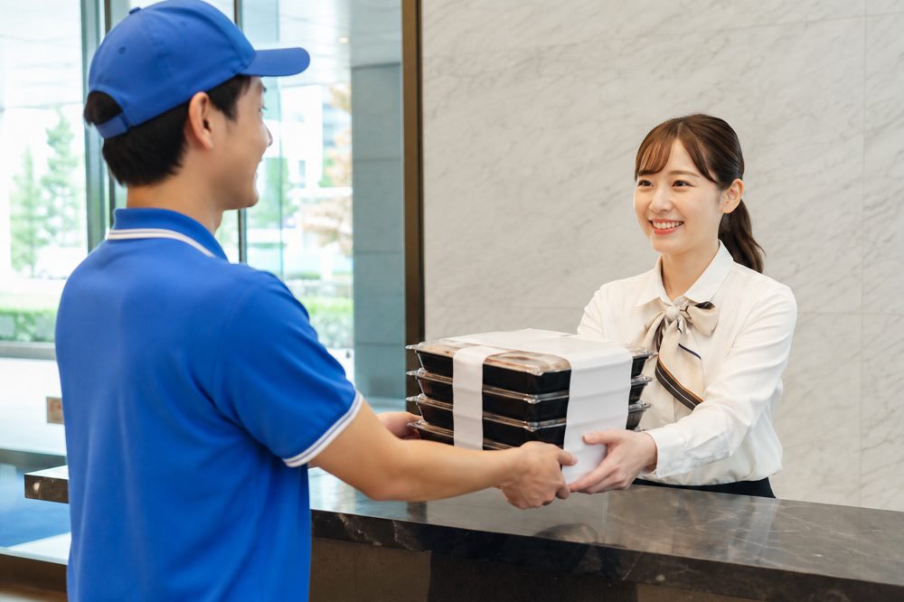広島のオフィスビル玄関で弁当を受け取る企業スタッフ