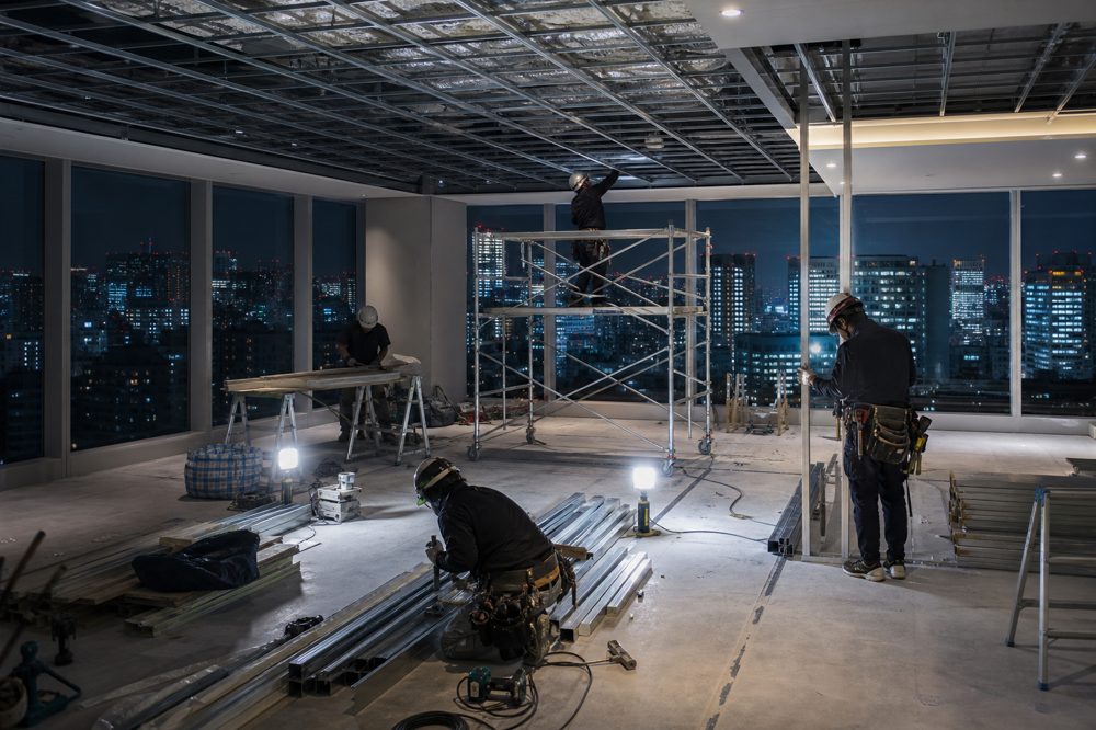 東京の高層ビルで夜間施工中のオフィスリノベーション現場・作業員と資材