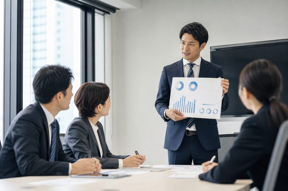 愛知の会議室で保険アドバイザーが中小企業チームにグラフ入り資料を提示している場面