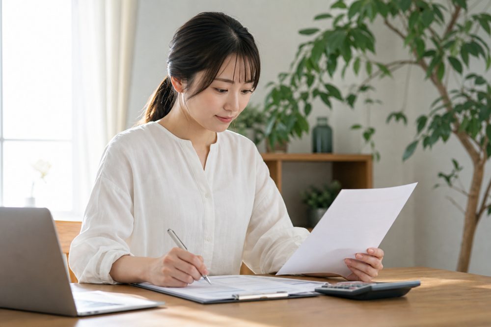 保険証券とチェックリストを確認する日本人女性の自宅デスク