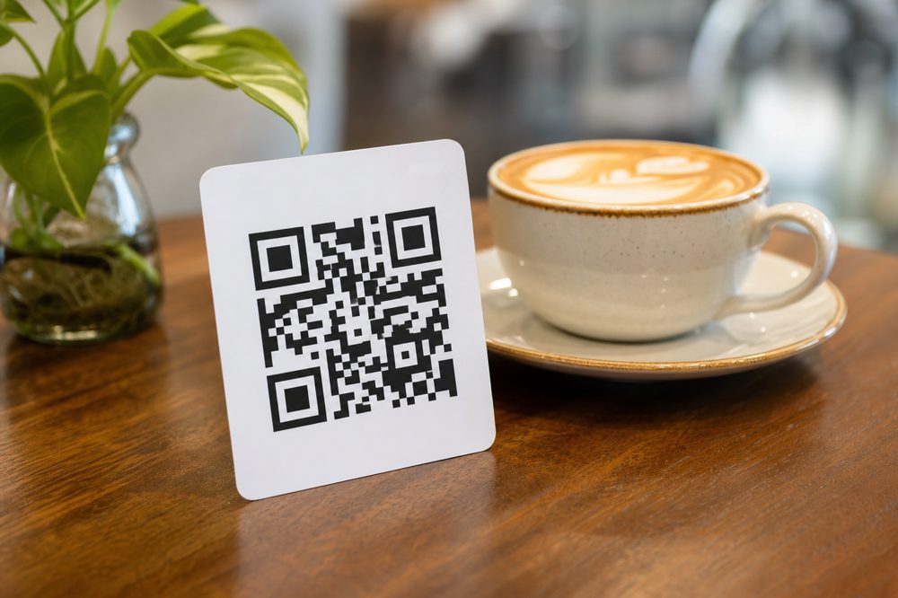 カフェテーブルにコーヒーカップと並んで置かれたQRコード口コミカードのクローズアップ