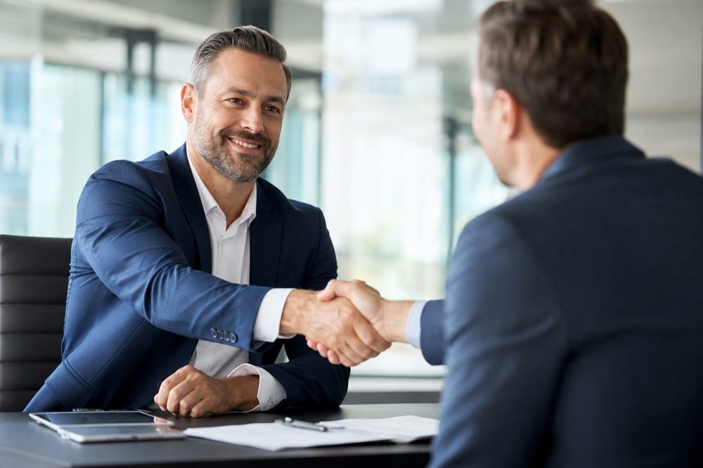 中小企業の経営者が資本提携の握手を交わしている場面