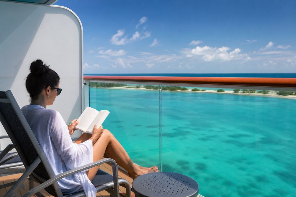 クルーズ船のバルコニーでターコイズブルーの海を眺めながら本を読む一人旅の旅行者