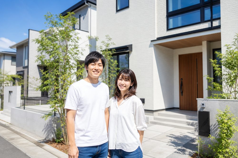 愛知県の新興住宅地で新築一戸建ての前に立つ笑顔の若い夫婦