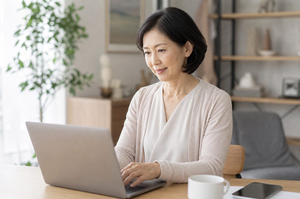50代の日本人女性が自宅の明るいデスクでオンライン証券口座を設定しているシーン
