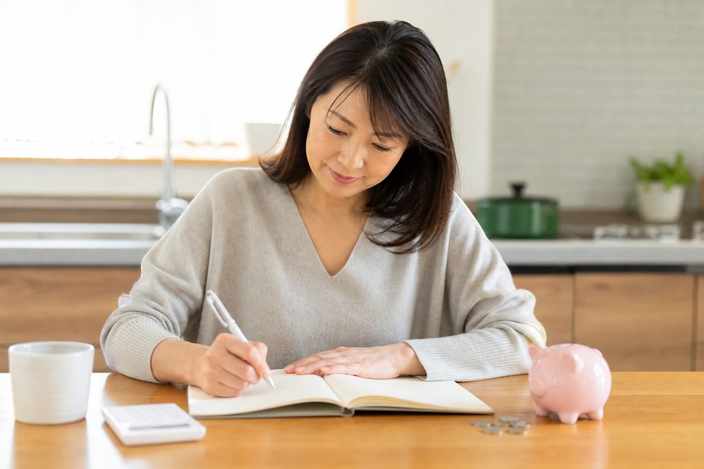 老後の資金計画を自宅でノートに書き込む40代日本人女性のイメージ
