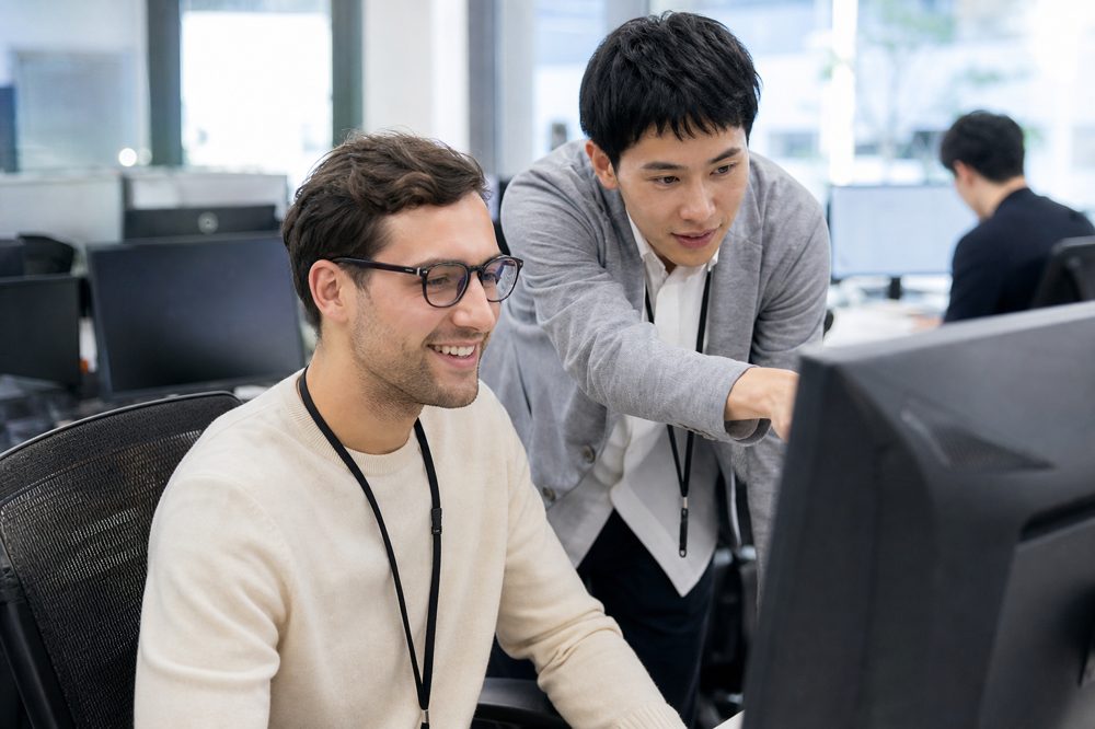 日本人社員から指導を受ける笑顔の外国人エンジニア