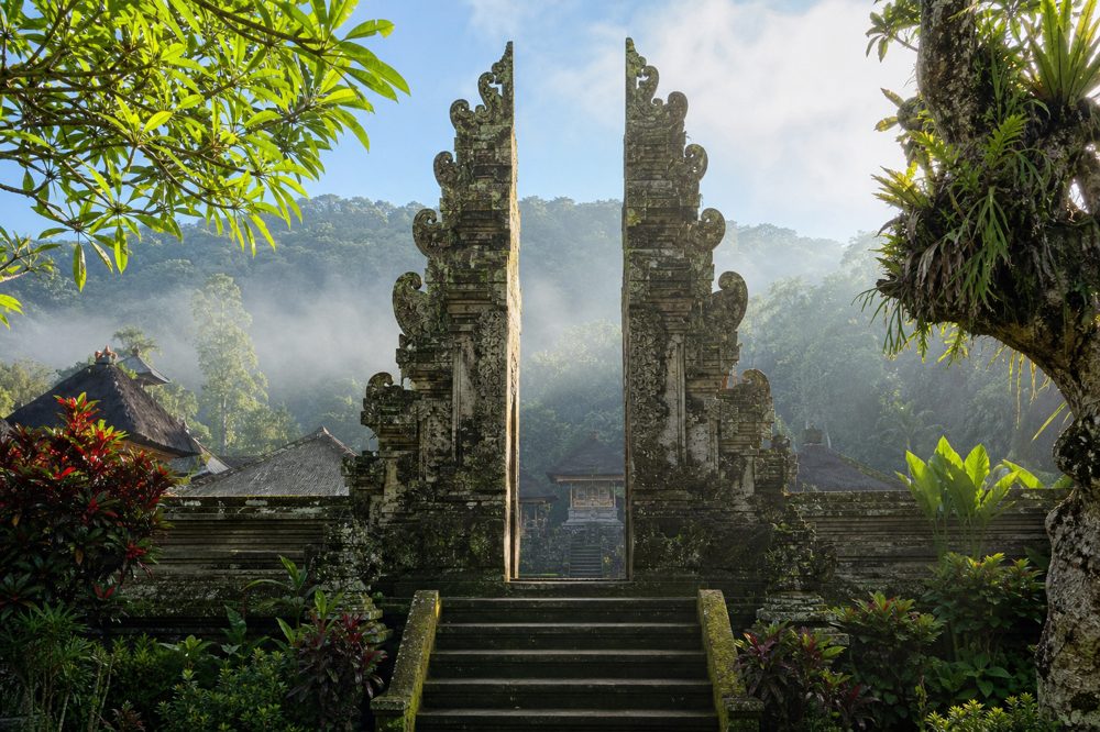 バリ島の伝統的な石造りの寺院門と熱帯植物に包まれた朝霧の風景