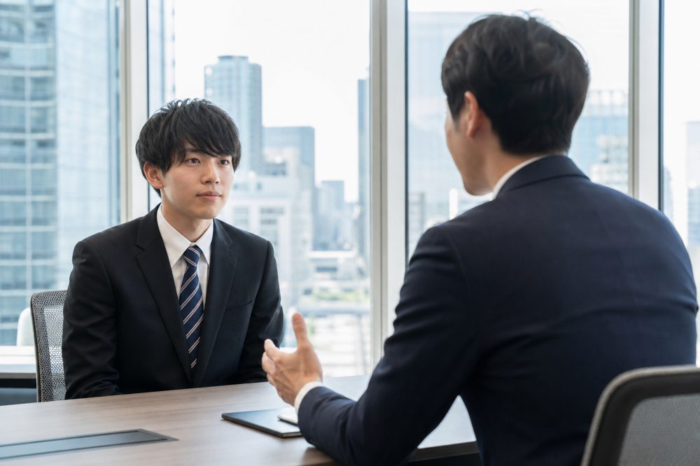 東京のモダンなオフィスで採用担当者と新卒ITエンジニア学生が1対1で面談している様子