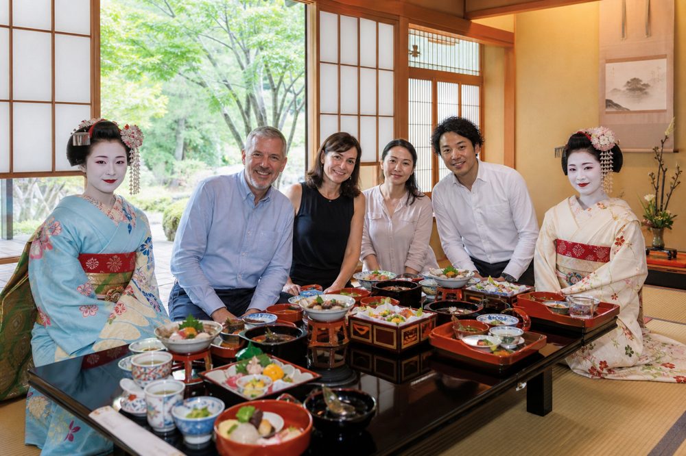 畳の座敷で舞妓が隣に座り懐石料理を楽しむ社員旅行の昼食