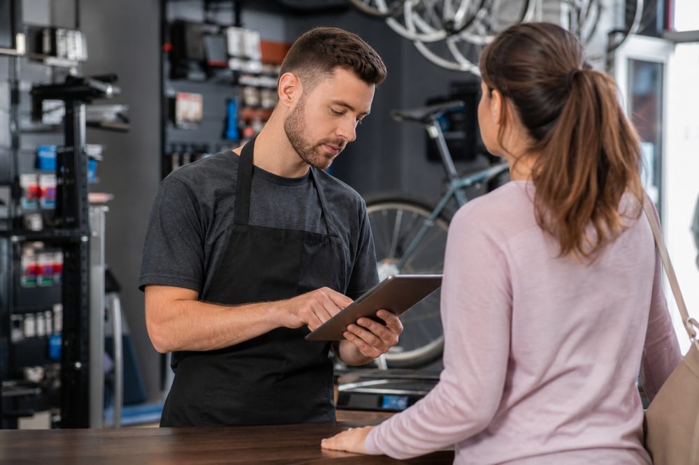 自転車販売店のスタッフがタブレットで顧客の整備履歴を確認している様子