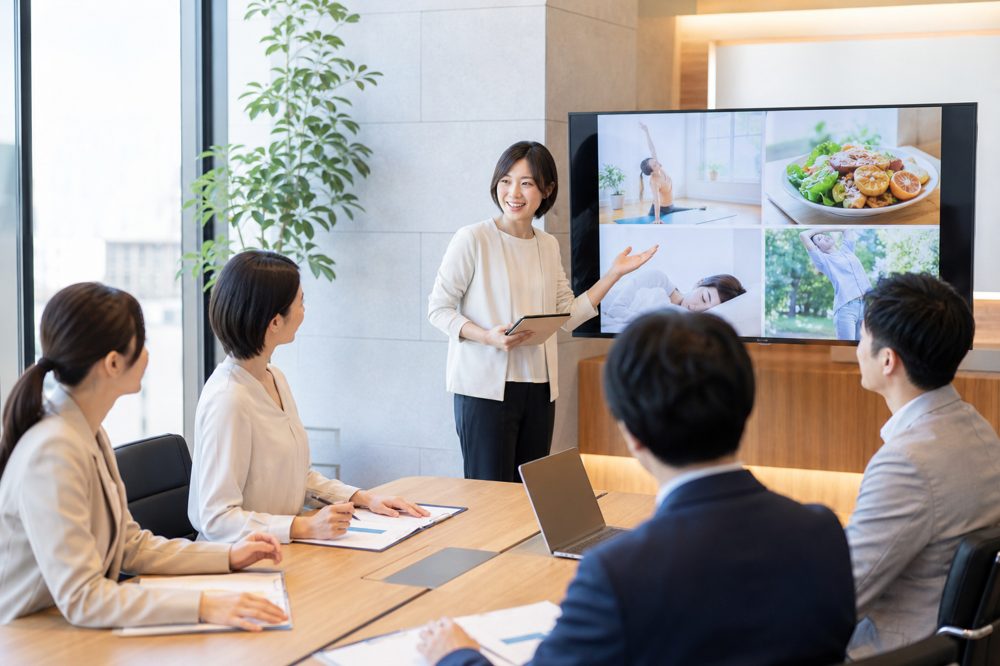 日本の現代的なオフィス会議室で人事マネージャーがウェルネスプログラムを提案している様子